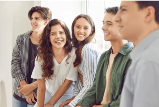 Un groupe de cinq jeunes souriants se tient côte à côte, certains regardant l'objectif, dans un intérieur lumineux.